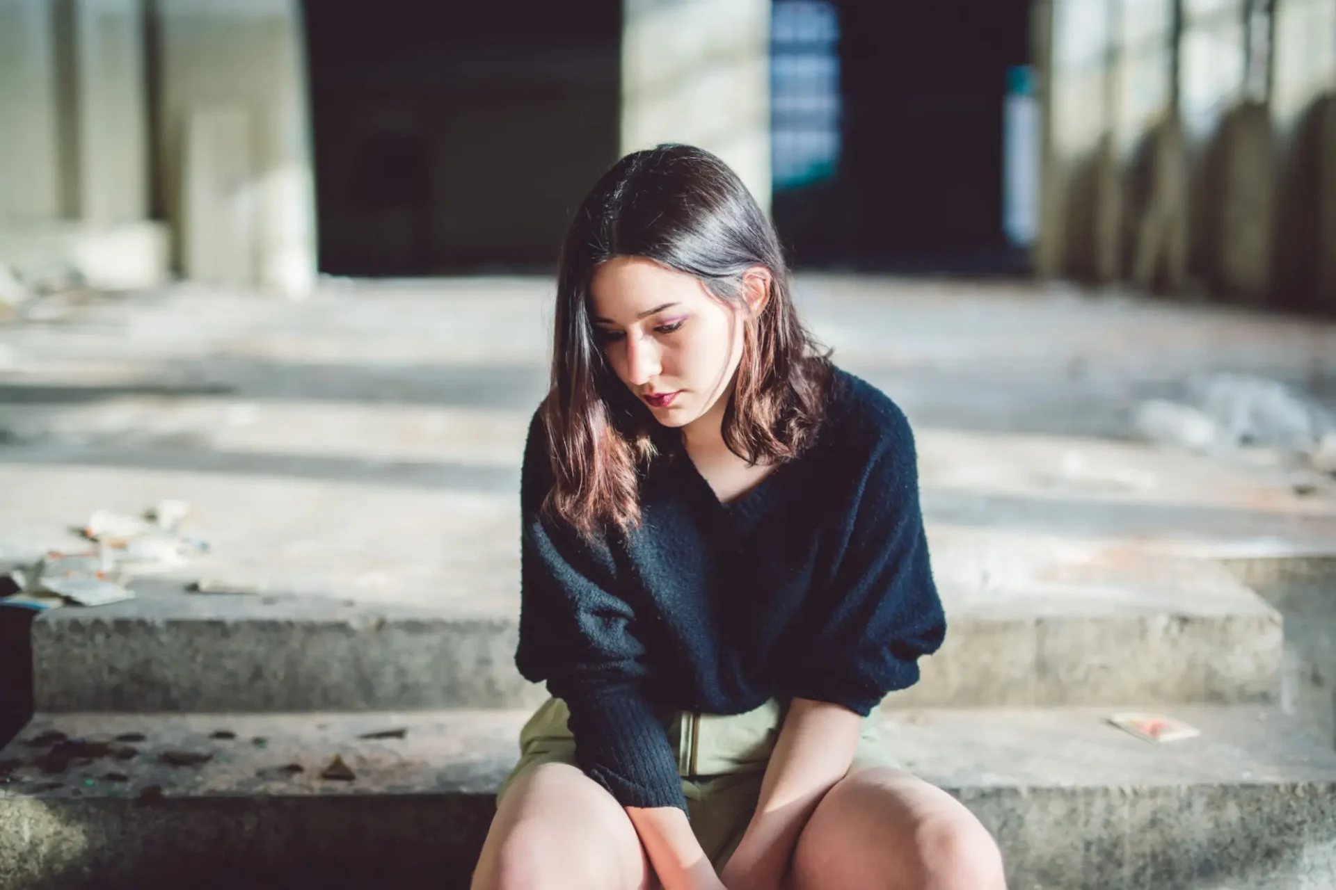 Young woman sitting alone on steps, looking downward.